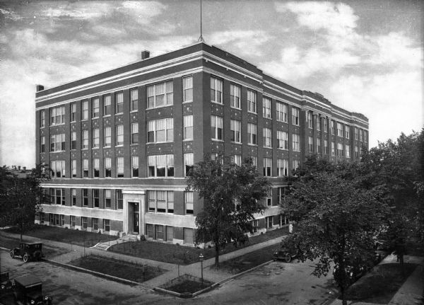 Elevated view of the five-story Home Economics Building at the Stout Institute (now University of Wisconsin-Stout). Automobiles park alongside the streets bordering the building.