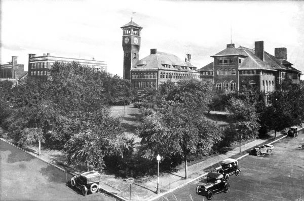 Elevated view of buildings on the Stout Institute campus (now the University of Wisconsin-Stout).  The buildings include a clock tower and are located on a lawn bordered by roads where automobiles park.
