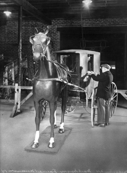 A mailman in a horse-drawn mail wagon makes a delivery to a man standing beside him in an exhibit at the Farmer's Museum.