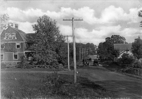 Cars travel past dwellings and power lines along a country road.