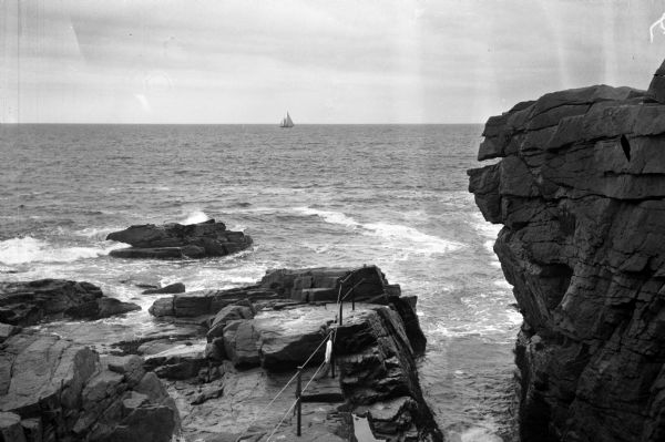 View looking from the rocky coastline toward a sailboat at sea.