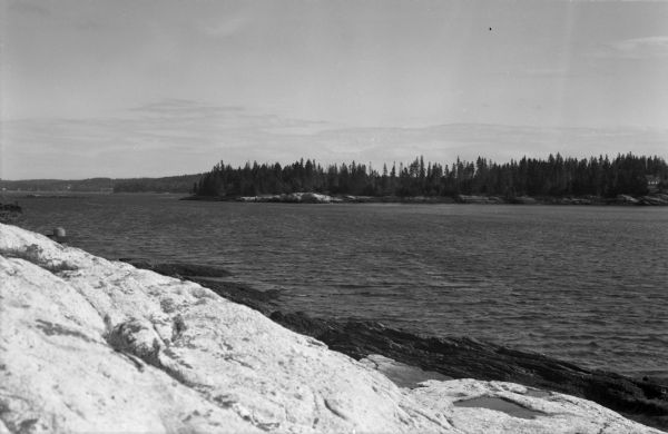 View from the rocks of the coastline looking toward the tree-covered opposing shore.