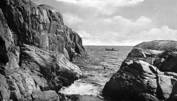A person rows a rowboat near the rocky cliffs at Gap Head.