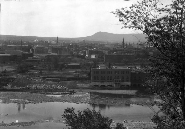 Elevated view of town buildings as seen from Bancroft Tower. A body of water and what appears to be an industrial plant are in the foreground.