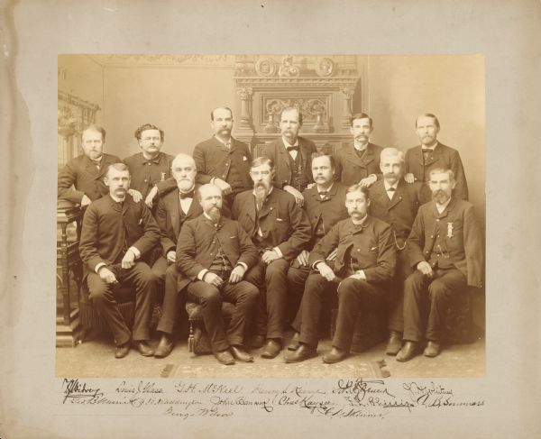 Group portrait of Civil War veterans who compiled the Roster of Wisconsin Volunteers for the Wisconsin Adjutant General's Office in the late 1880s. Back Row: Theodore J. Widvey, Louis Glass, G.H. McNeel, Henry S. Keene, James F. (?) Spencer, J.H. Whitney (?);  Middle Row: George B. Merrick, L.B. Waddington, John Hancock, Charles Kayser, F.L. Phillip, D.B. Sommars (or J.B.); Front Row: George Wilson,  C.D. Skinner 