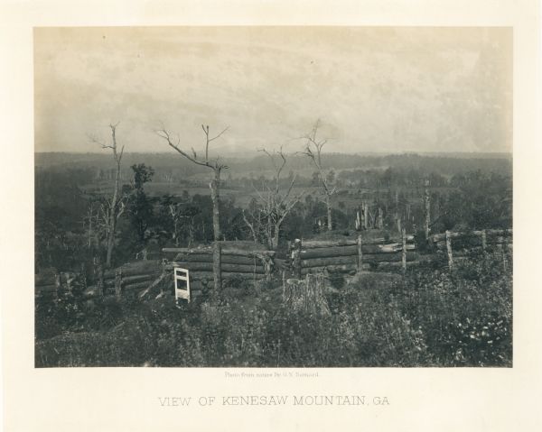 A fence or battlement, with battered trees overlooking a valley. Kenesaw Mountain is in the distance.
