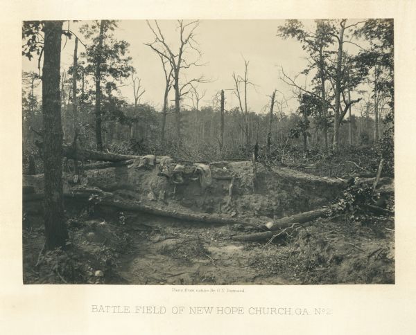 An earth mound with some burlap sacks covering it. Many barren trees surround the scene.<br>Plate 26</br>