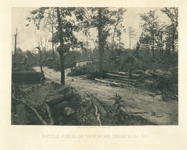 A dirt road passes through the battlefield, with fortifications on the sides. It is a lightly forested area. A horse and buggy are among some trees in the background.<br>Plate 25</br>