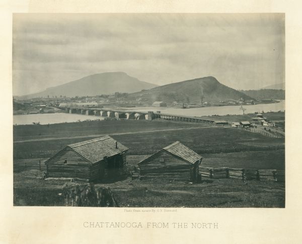 Two log buildings are in the foreground. A bridge spans a river in the middle distance, and the city of Chattanooga is on the far side at the base of a mountain.<br>Plate 08</br>