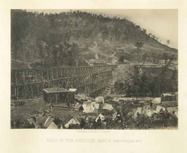 Union soldiers stand by their tents in front of a trestle bridge on the railroad line that spans a valley. A mountain is in the background.<br>Plate 06</br>