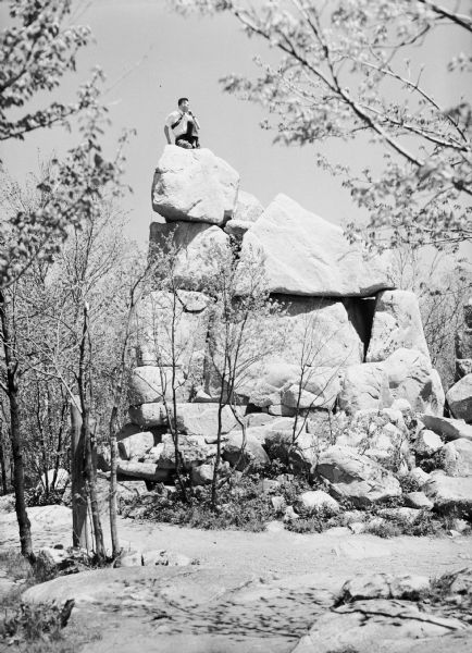 View from below of a man, sitting atop a large rock pile/quarry in the vicinity of Wausau.