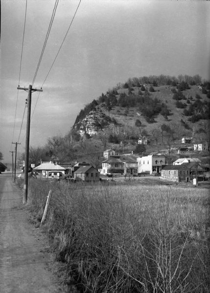 View along side of road across a field of a village on the Mississippi bluffs, with many houses and telephone lines visible.