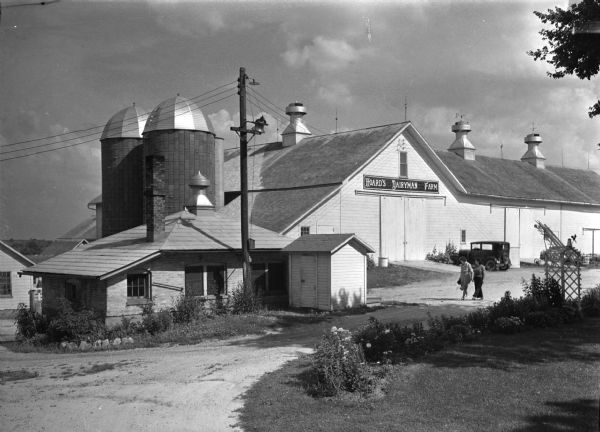 A model dairy farm maintained by Hoard's "Dairyman Magazine" for experimental purposes. Two women are walking in the driveway near the buildings on the right.