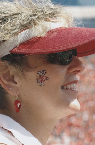 Female Badger fan with a temporary tattoo of Bucky Badger on her cheek. She is seen in profile at a University of Wisconsin-Madison football game.
