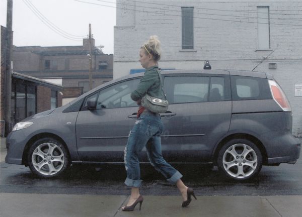 Woman in heels walking past a parked car on foggy day.