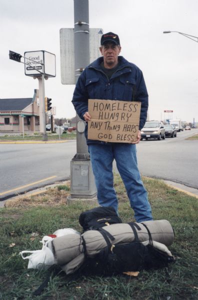 A homeless man holding a cardboard sign that reads "HOMELESS HUNGRY ANY Thing HELPS GOD BLESS" on Rose Street intersection.
