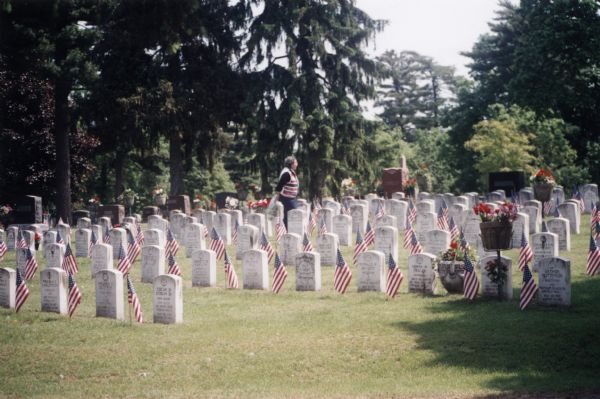 A woman walking in Oak Grove Cemetery on Memorial Day. American flags stand at each headstone of past soldiers.