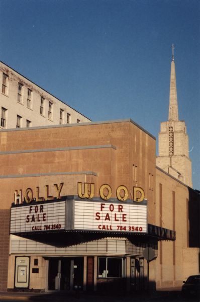 The marquee at the defunct Hollywood Theater reads "for sale." A church steeple is in the background.