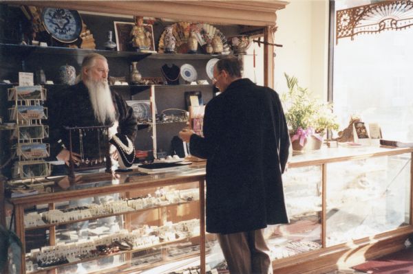 Man looks at jewelery at variety store, while John Satori standing behind the counter.