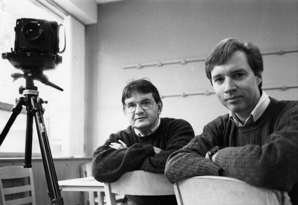 Gary MacDonald (left) and Roger Grant (right), photography professors at University of Wisconsin-La Crosse, posing alongside a camera.