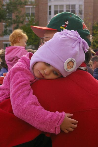 A young child, held in her father's arms, wearing an "Obama Baby" pin on her hat.