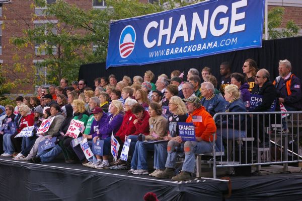 Seated Obama supporters hold American flags and signs, and a "Change" banner hangs behind them.