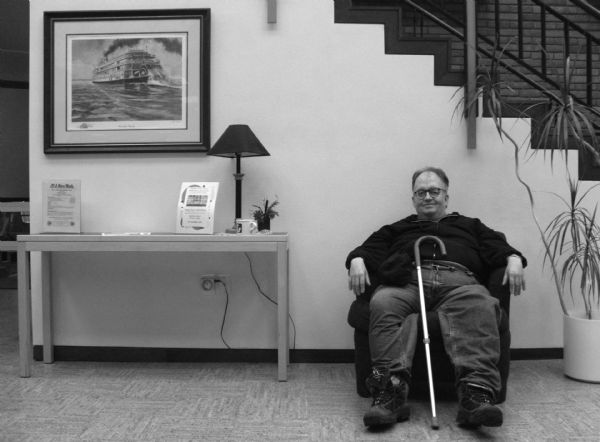 Aquinas High School archivist, Richard Dungar, sitting in a chair near a painting of "Delta Queen."