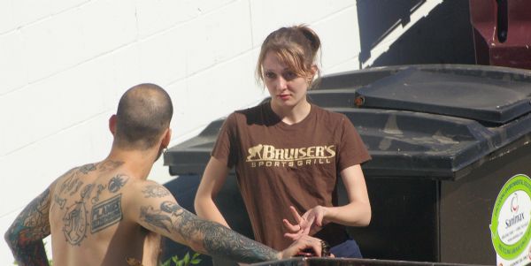 "Bruiser's Sports grill" employee talking outdoors with a shirtless, tattooed man by dumpsters.
