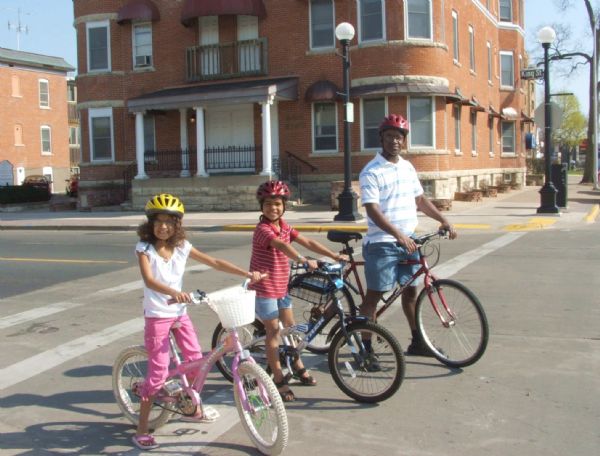 Father and two children stopped at an intersection while on a bike ride.