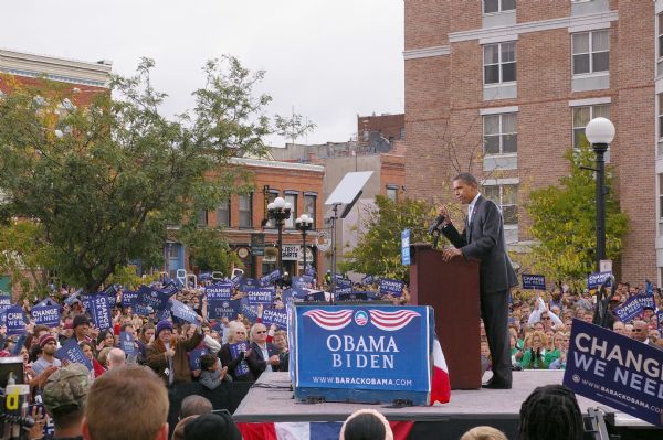 President Barack Obama speaking at rally. Members of the crowd are raising their signs in support.
