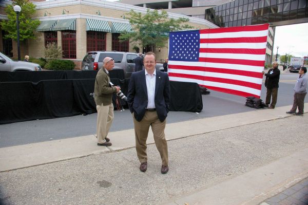 Press Secretary Robert Gibbs posing outside the Barack Obama rally. An American flag is in the background.