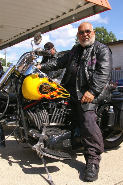 A biker wearing a leather jacket with patches and pins of the Christian cross. On his motorcycle, a quotation reads: "Deuteronomy 4:24 - For the Lord your God is a consuming fire, a jealous God."