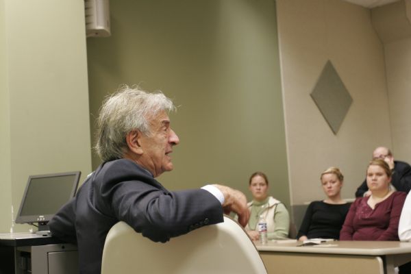 Holocaust survivor Elie Wiesel speaking.  A group of people are sitting and listening in the background.