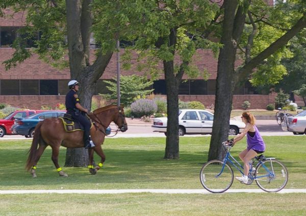 A female bike rider looks over at police officer riding a horse at Riverside Park.