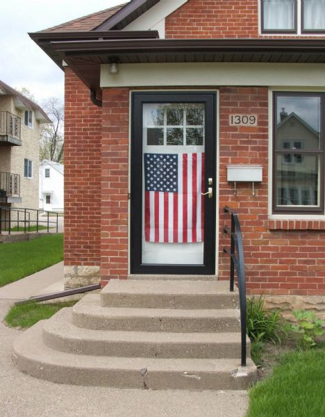 An American flag is hanging on the front door of a red brick house.