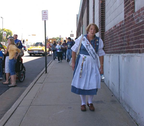 Kathy Vehrenkamp, Mrs. Oktoberfest 1991, walking down the sidewalk in costume and proudly displaying her ribbon.