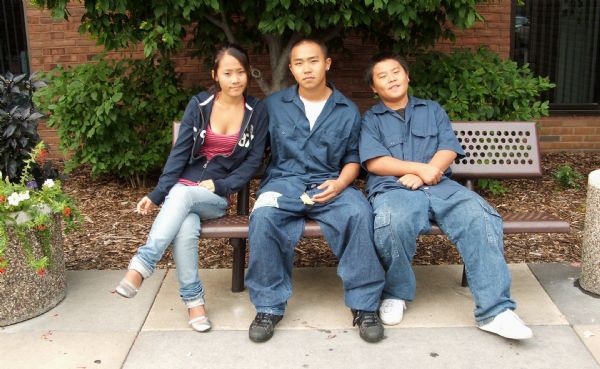 Three Hmong teenagers posing for a group portrait sitting on a bench.