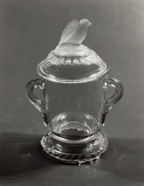 Old Abe covered glass compote made by the Crystal Glass Company of Bridgeport, Ohio.  Exhibited at the Centennial Exhibition in Philadelphia in 1876 where the real Old Abe was a major attraction as well.  

The set included three sizes of compotes, a covered butter-dish, a covered sugar bowl, a spoon holder, a cream pitcher and a salt dish.  Only the compotes, butter dish and sugar bowl had the eagle finial.  The other pieces carried out the pattern with the rope and stylized claws.  The rope is believed to represent the cord by which Old Abe was fastened to the perch at the top of the staff.  

This is housed in the collections of the State Historical Society of Wisconsin museum with the accession number 1961.139a.
