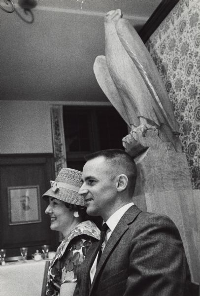 Basswood carving of an eagle, inspired by "Old Abe" of the Civil War 8th Wisconsin Volunteer Infantry, in the American Club Restaurant of the Kohler Company.  A man and a woman are seated posing in front of the carving and a set table is visible in the background.