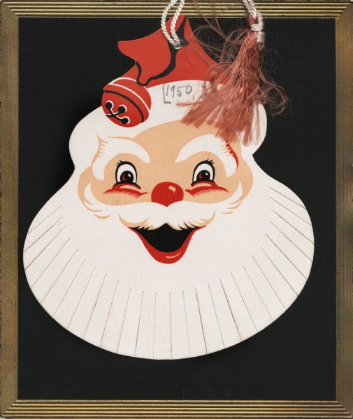 Holiday card of a die cut head of Santa Claus and a gold edged, embossed, black, square card. There is a hole at the top of both pieces with a tasseled string tying them together. Santa has a die cut beard and a bell on his hat. When you move Santa to the side the greeting "Merry Christmas and a Happy New Year" can be seen. Letterpress, black, gold, red and flesh tone inks.