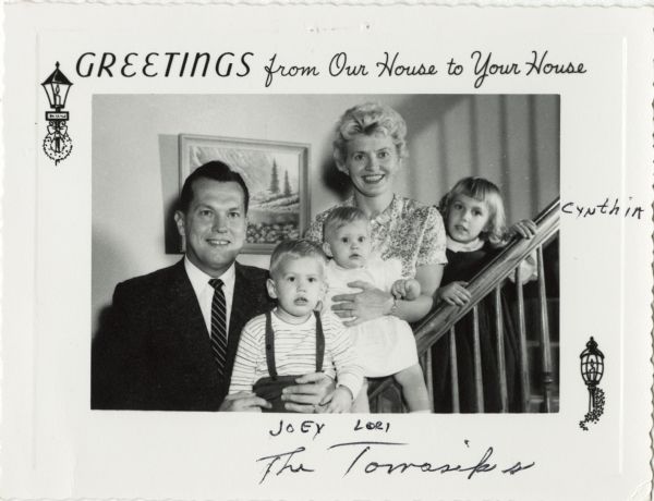 Photographic holiday greeting card of a family posed on their staircase. A father, mother, two daughters and one son are pictured. At top is the text "Greetings from Our House to Your House'.