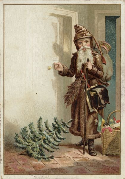 Holiday card of Santa Claus knocking on a door in a hall with a brick floor. He is wearing a brown coat and hood, with a sack of toys on his back, a basket of toys at his feet and a slate and bag slung over his shoulder. He is holding a walking stick and has a bundle of switches in his belt for naughty children. An untrimmed Christmas tree is on the floor at this feet. The image has a gold and white border. Chromolithograph and embossed.