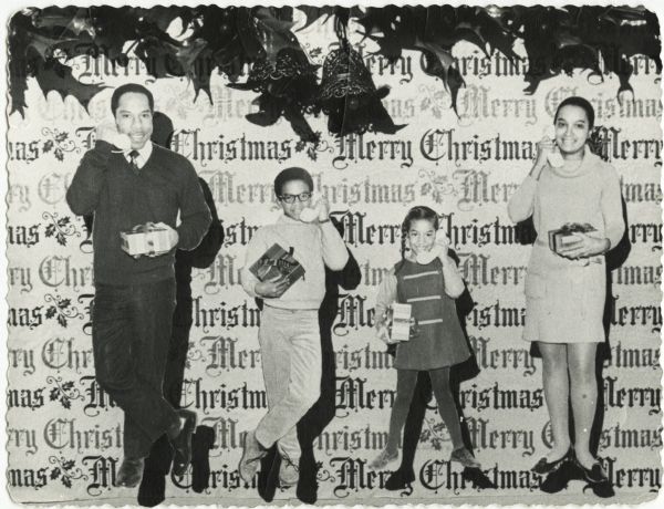 Photographic holiday card of an African American family posed over "Merry Christmas" wrapping paper in the background. Holly and bells appear overhead. Each of four family members holds a wrapped gift and is talking on the telephone. The family is that of George Haley.