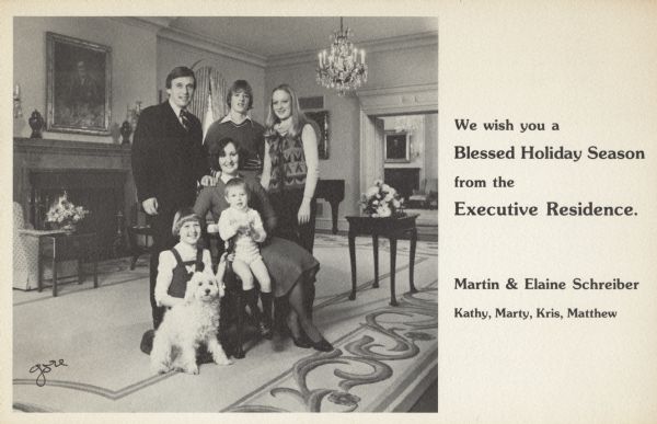 Photographic holiday card from Governor and Mrs. Martin Schreiber and family, governor of Wisconsin 1977-1979. The front of the card is an image of the family in the executive residence. It reads on the right side: "We wish you a Blessed Holiday Season from the Executive Residence." The names of the entire family are below. Offset lithography.
