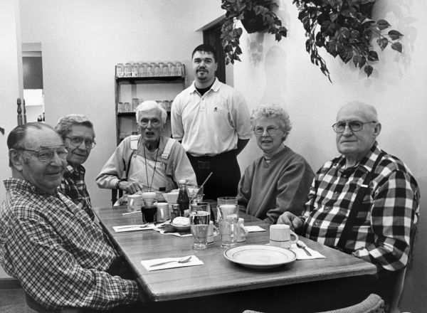 "Fish Fries are very reasonable at the Back Street Cafe. Red Fish (similar to Perch) are only $4.95. A large glass of Slice is 45¢. Our waiter is Brock Cotter." From left to right; Rudy Heinecke, Ralph "Buddy" Ruecker, Ralph Widmer, Brock Cotter, Shirley Widmer, and John Bodden.