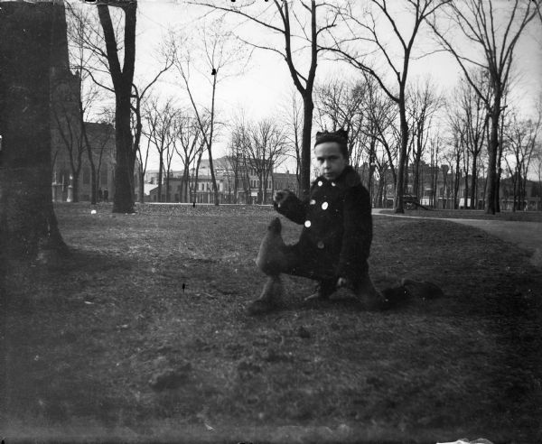 Forest Middleton offers a treat to a squirrel, who is sitting on his knee. They are in Capitol Park; Grace Episcopal Church is in the background on the left. Commercial buildings line Carroll Street.