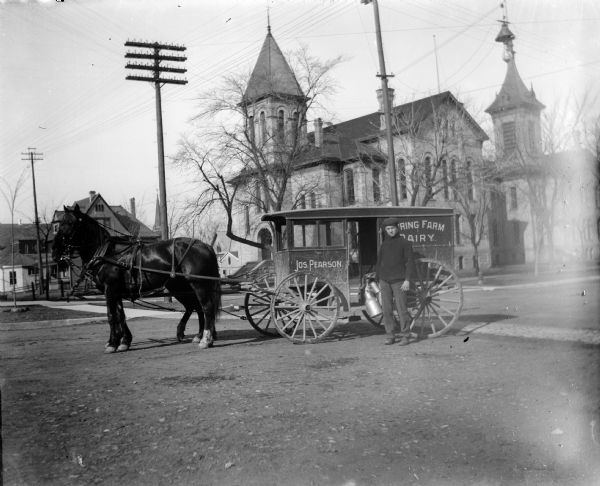 Joseph Pearson, milkman, poses with his wagon and team of horses in front of the Madison High School at the corner of Wisconsin Avenue and Johnson Street.