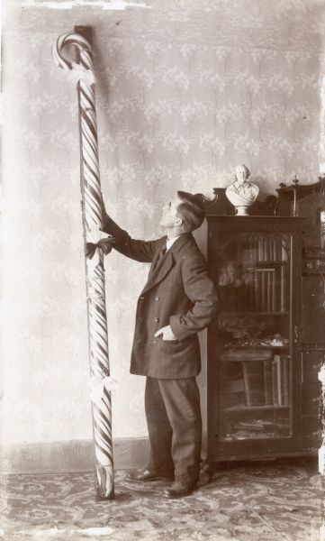 William Elwell Middleton stands beside the giant candy cane which he won on Christmas Day, 1909. There is a bookcase in the background.