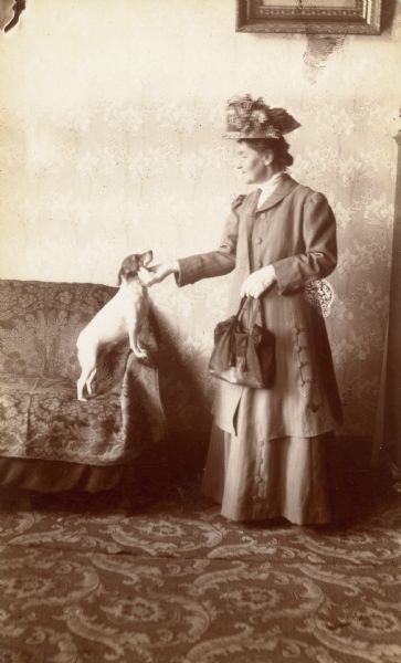 Clara Middleton, well-dressed and wearing a large hat, holding her pet fox terrier's chin as the two share a gaze.