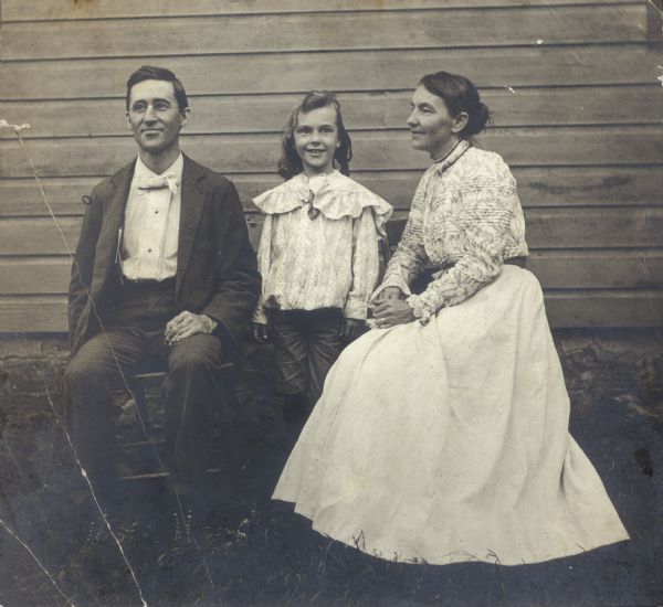 William and Clara Case Middleton sit on chairs alongside a building; their son Forest stands between them.